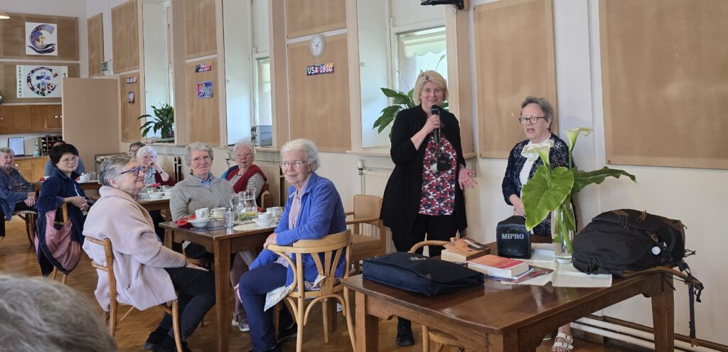 Luxeuil Pilgrims9 - Columban Missionaries Seniors seated at tables in a bright room while a woman speaks into a microphone at the front.