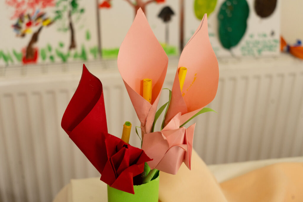 Bright paper flower sculpture with pink and red petals in a lime green vase, colorful crafty background blur.