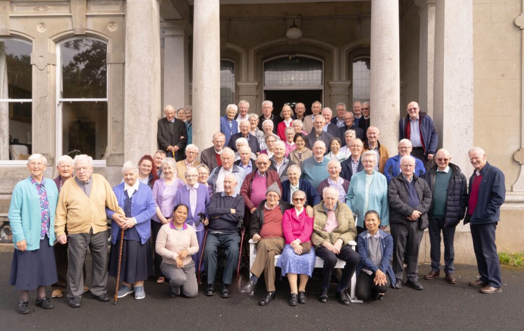 Large group of elderly people standing on steps in front of a stone building with columns, posing for a photo.